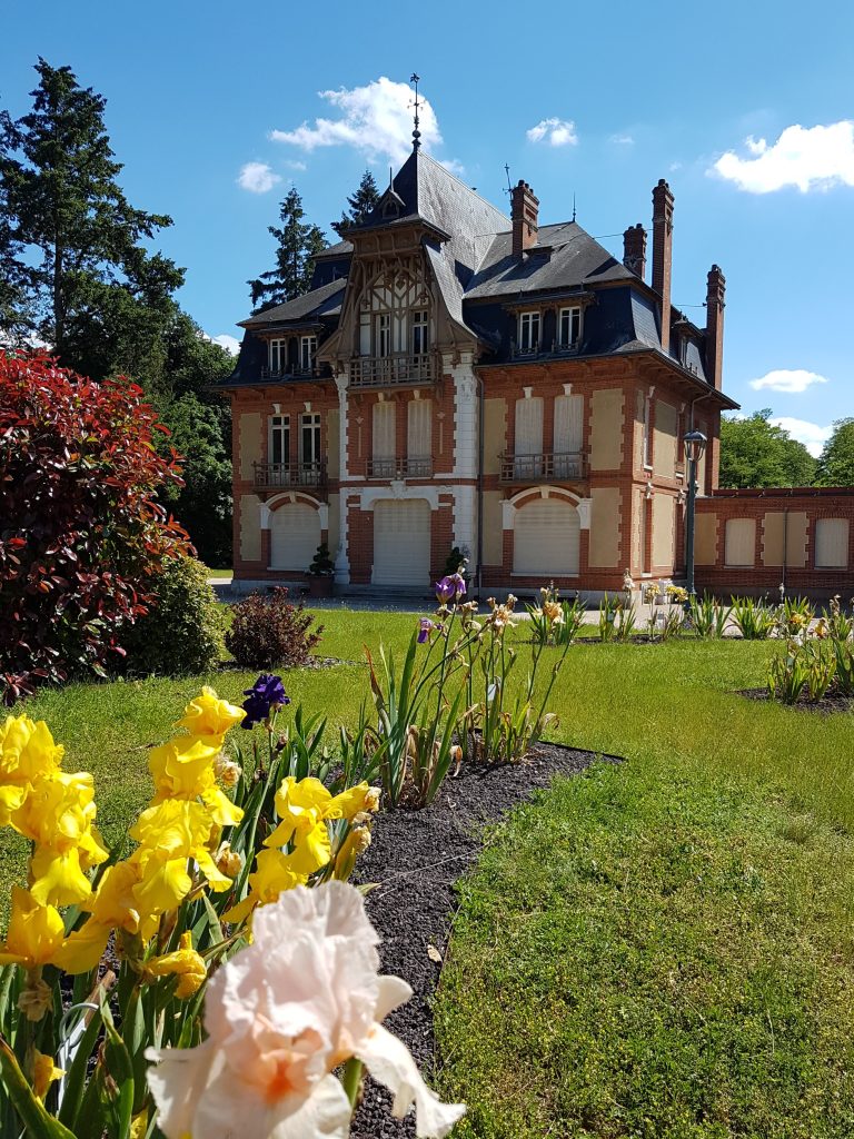 La façade du château de Morchêne derrière un massif d’iris jaunes et violets
