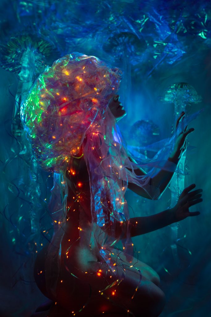 Une femme couronnee d une meduse translucide constellee de lumieres colorees, dans une eau bleu profond