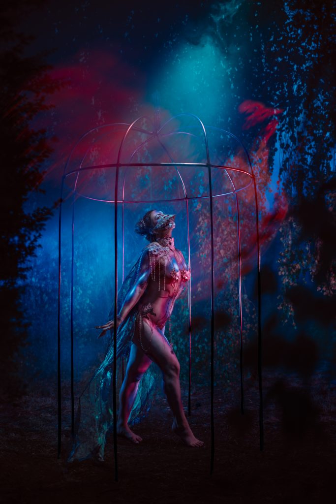 Une silhouette debout sous une grande structure en forme de meduse, eclairee de rouge et de bleu dans un sous-bois nocturne